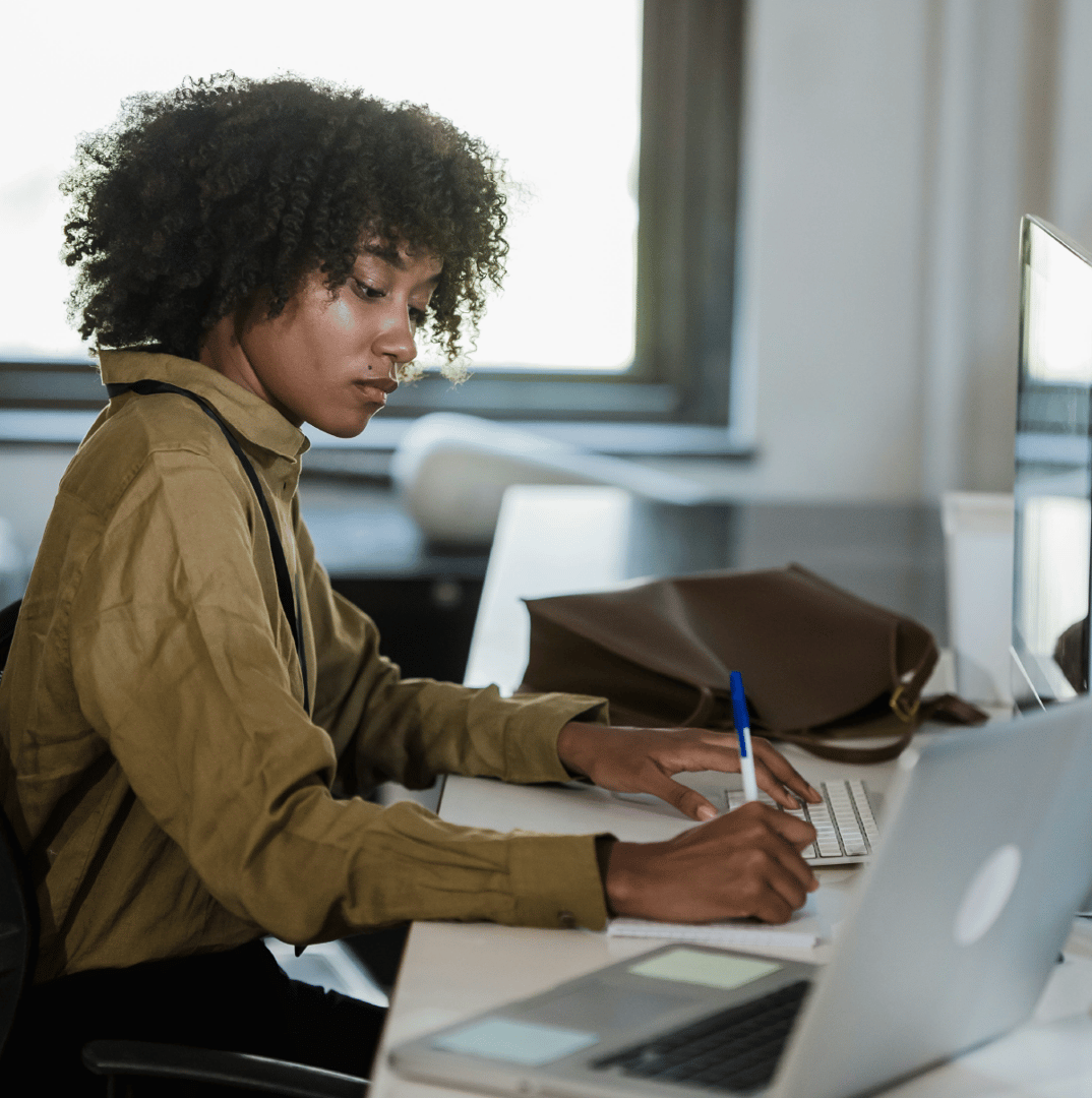 Young professional working at a laptop by a bright window, focused on typing